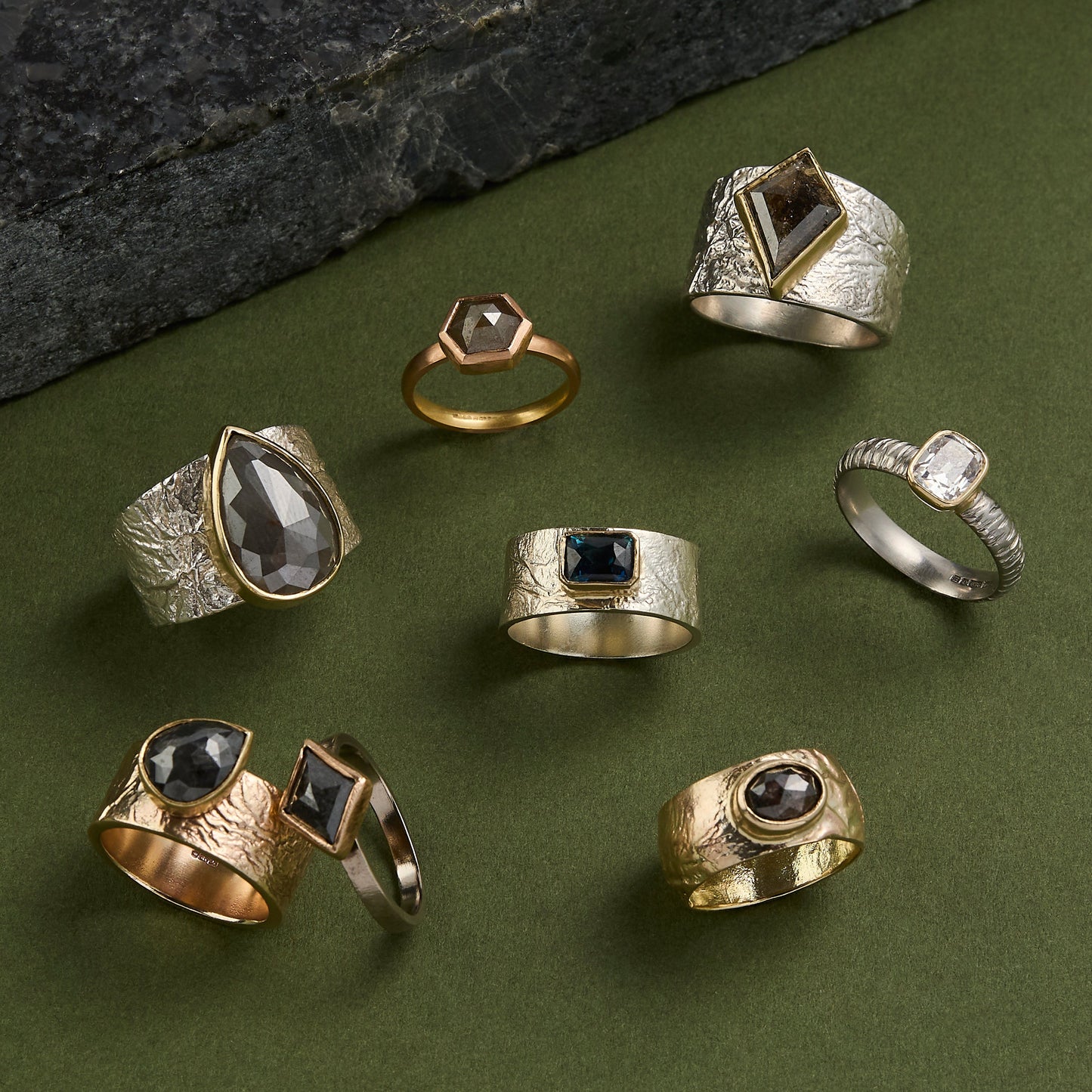 Collection of various rings with different designs on a green surface.