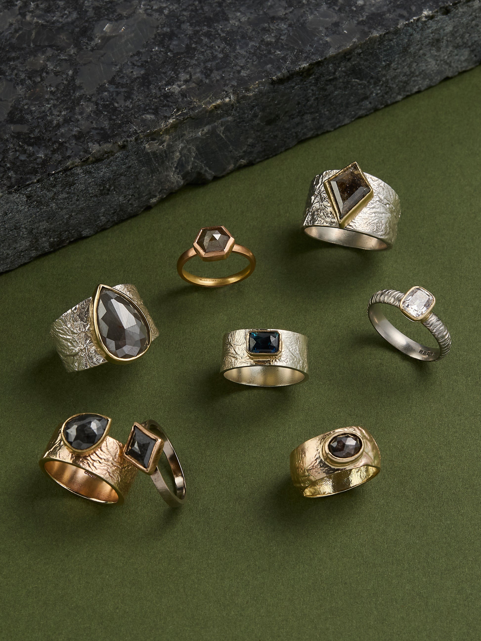 Collection of various rings with different designs on a green surface.